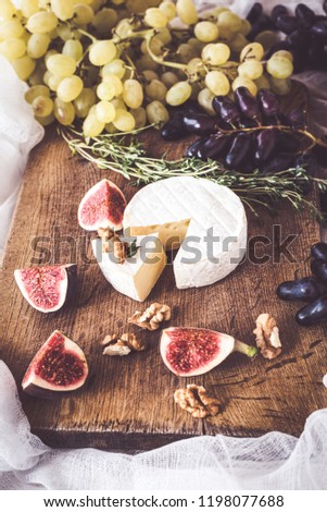 Top view of a wooden stand with Camembert cheese, grapes, nuts and figs with a bunch of oregano,. Vertical banner
