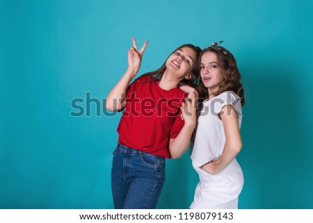 Full height image of two happy cheeky girls , best friends having fun , laughing on blue background. . Wearing stylish casual clothes. Space for text. Cute teenage school girls