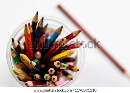 Color pencils in a glass on a sheet of white paper.