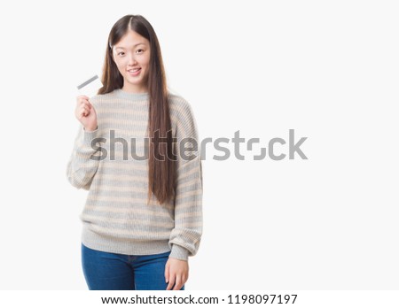Young Chinese woman over isolated background holding credit card with a happy face standing and smiling with a confident smile showing teeth