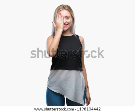Young blonde woman over isolated background covering one eye with hand with confident smile on face and surprise emotion.