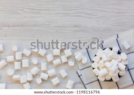 Fluffy marshmallows in a bowl over white wooden background, top view. Flat lay, from above, top view. Copy space. 
