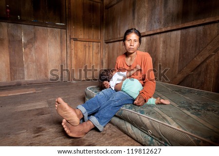 A poor mother in America sits by the Amazon river, breastfeeding her baby in distress. Dark faces of poverty surround her family. Royalty-Free Stock Photo #119812627