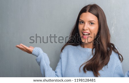 Young brunette woman over grunge grey wall very happy and excited, winner expression celebrating victory screaming with big smile and raised hands