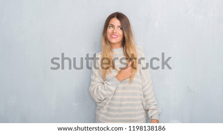 Young adult woman over grunge grey wall wearing winter sweater with a big smile on face, pointing with hand and finger to the side looking at the camera.