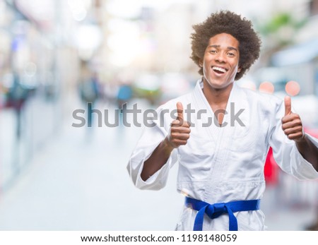 Afro american man wearing karate kimono over isolated background success sign doing positive gesture with hand, thumbs up smiling and happy. Looking at the camera with cheerful expression, winner