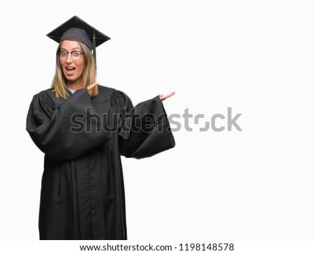 Young beautiful woman wearing graduated uniform over isolated background amazed and smiling to the camera while presenting with hand and pointing with finger.