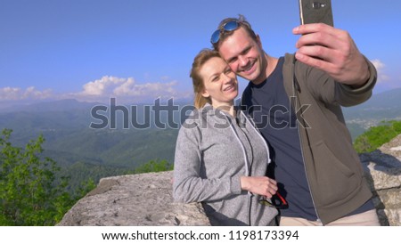 a couple, a man and a woman do a sefi with a view of the Magnificent Mountains.