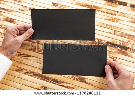 Mens hands holding empty black flyers on bamboo background. Blank paper mock-up