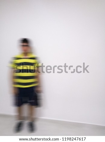 Young man dressed in black shorts with yellow striped shirt defocused and moving with an intentional blur to give a concept of ghost, disappearance, spectrum, action or motion.