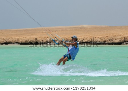 Kite surfing man surf sportsman with kite in sky on board in blue sea riding waves with water splash. Recreational activity, water sports, action, hobby and fun in summer time. Kiteboarding sport