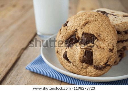 Close up picture of chocolate cookies in white plate on blue stripe napkin and a cup of milk on wooden plank table
