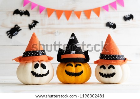 White and yellow ghost pumpkins with witch hat on white wooden borad background with bat. halloween concept.