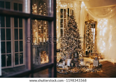 warm cozy evening in Christmas room interior design,Xmas tree decorated lights gifts, deer,candles, lanterns, garland lighting indoors fireplace.holiday.magic New year.open door to fairy tale 