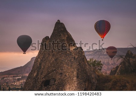 Early in the morning captured flying hot air balloons from highest point in Gorome. Many of balloons rise above the beautiful landscape of Cappadocia Valley in dramatic foggy sky.