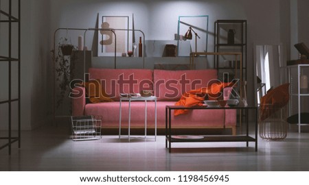 Night view of powder pink sofa with orange pillow and blanket in the middle of art collector's apartment full of metal shelves and abstract paintings, real photo made