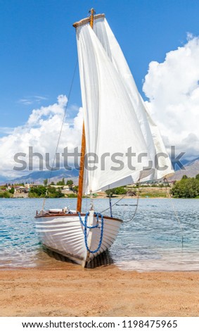 Boat with a white sail on the sandy beach.
