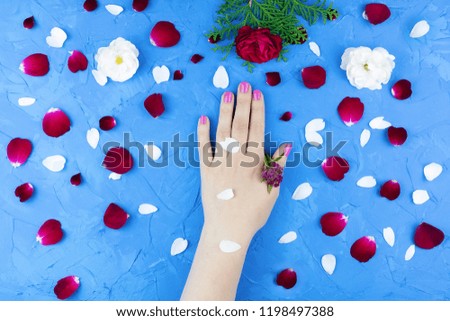Beauty gentle hands with flowers and flower petals on blue background, hands with beautiful bright makeup and rose petals, Valentine's day