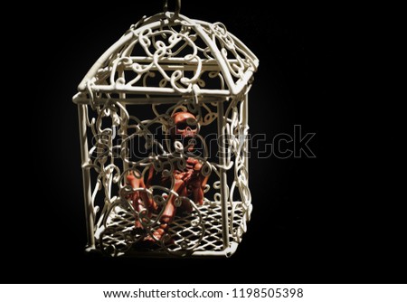 Skeleton in white cage on black background.