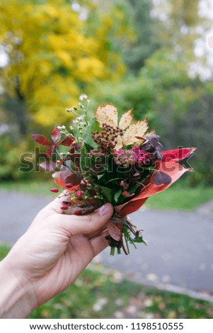 Autumn mini bouquet of yellow and orange flowers, red berries and leaves in woman hand