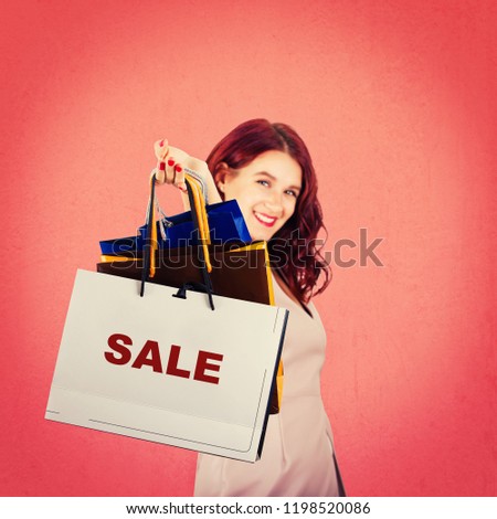 Excited young woman smiling with hand stretched forward holding paper shopping bags isolated over red background. Sale for christmas holiday.