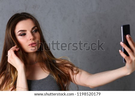 Beautiful european woman portrait. Worth a gray background uses a smartphone makes selfie and reads messages from social networks and messengers