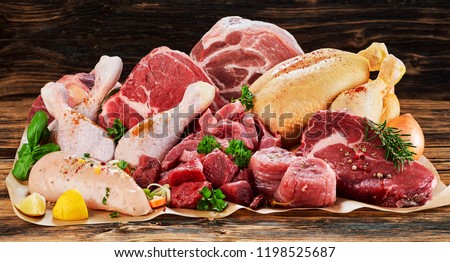 Raw meat assortment, beef, chicken, turkey, decorated with greens and vegetables, placed on cooking paper on wooden table Royalty-Free Stock Photo #1198525687