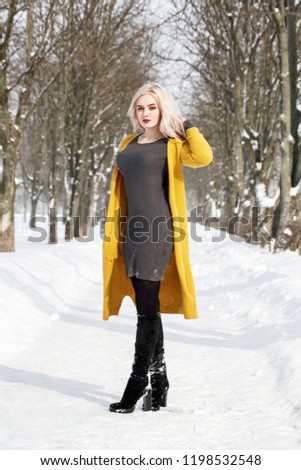 Full-length portrait of a young female model blonde in winter dressed in a yellow knitted sweater. Woman posing in a winter park.