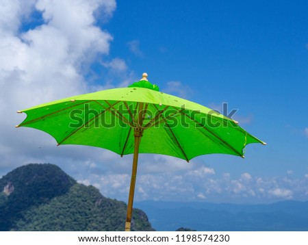 Close-up photo of green big umbrella on beautiful blue sky and mountains background.