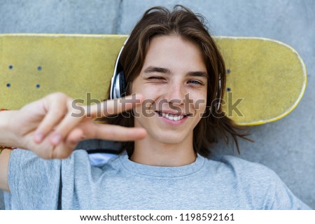 Top view of a cheerful young teenge boy spending time at the skate park, laying on a skateboard at a ramp, listening to music with headphones