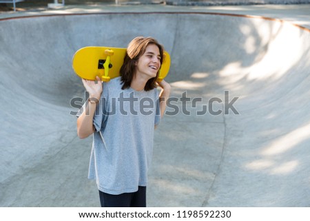 Cheerful young teenge boy spending time at the skate park, holding a skateboard
