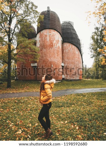  A girl with long hair in a bright yellow jacket stands against the background of a stone brick Church of the evangelists, built a strange shape, unusual Church, autumn leaves everywhere