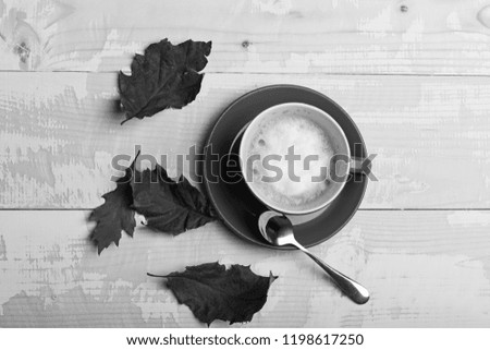 Autumn coziness concept. Warm and cozy autumn coffee time. Red ceramic tableware with tasty beverage, top view. Cup of cappuccino coffee on wooden background with autumn leaves.
