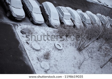 Cars covered in snow on a parking lot in the residential area during snowfall