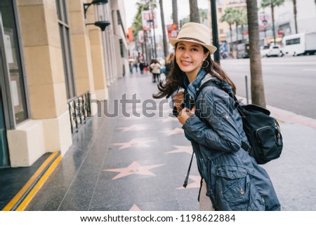 female traveler wearing straw hat and joyfully walking on the street. young backpacker face camera smiles exciting. attractive lady living a happy lifestyle shopping during USA vacation.