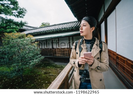 attractive woman walking through the garden while chatting with her friend on the cellphone. Self-guided trip concept with traveler reading online guidebook. Travel in Kyoto.