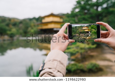 focus photo of someone taking picture of the Japanese golden temple by smartphone. traveler photographing when sightseeing. sightseeing tour concept.