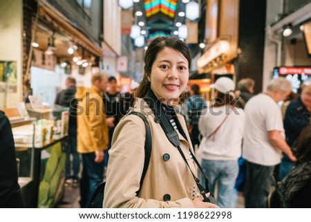 pretty female photographer face to camera smiling attractively while taking pictures in the traditional market. attractive woman standing in crowd. spring holiday travel in Japan.