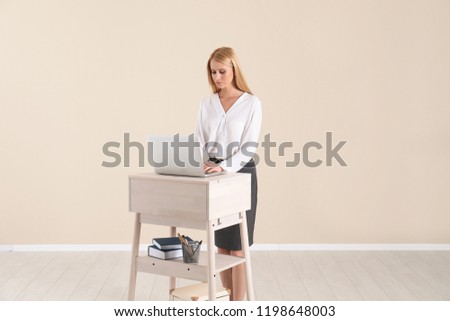 Young woman using laptop at stand up workplace against light wall
