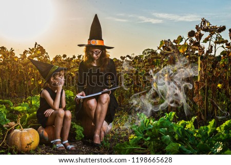 Mom and daughter in costumes of a witch are sitting on pumpkins and reading a book, concept of Halloween. Family is preparing for the holiday Halloween. Halloween background, free space.