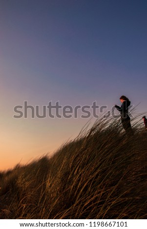 girl with cell phone in hand taking photo of sunset on the beach