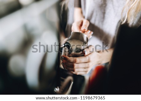 A youthful slim pretty blonde girl,dressed in casual outfit, is holding a milk frother in a cozy coffee shop.