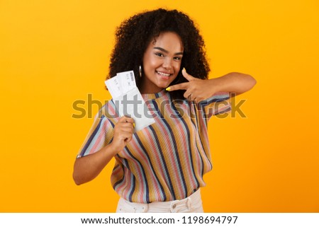 Picture of excited happy african woman posing isolated over yellow background holding passport with tickets.