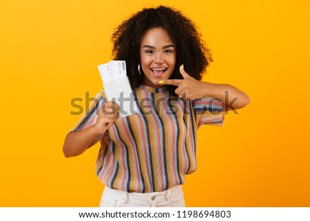 Picture of excited happy african woman posing isolated over yellow background holding passport with tickets.
