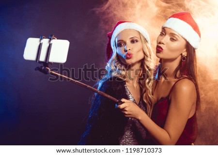 beautiful women in santa hats with kiss grimace taking selfie on smartphone