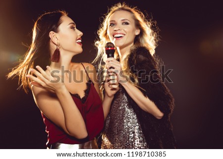 smiling attractive women dancing and singing with microphone in karaoke