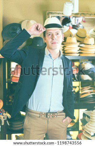 portret of cheerful european young guy try on  panama at headwear store
