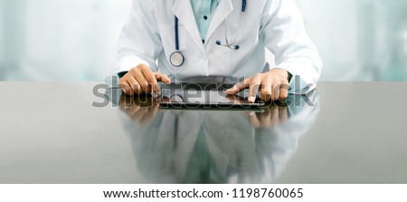 Male doctor sitting at table with tablet computer in hospital office. Medical healthcare staff and doctor service. Royalty-Free Stock Photo #1198760065