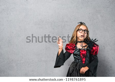 Blonde child dressed as a vampire for halloween holidays standing and thinking an idea on textured background