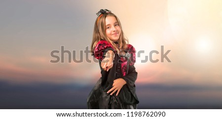 Blonde child dressed as a vampire for halloween holidays points finger at you at outdoor with sunset